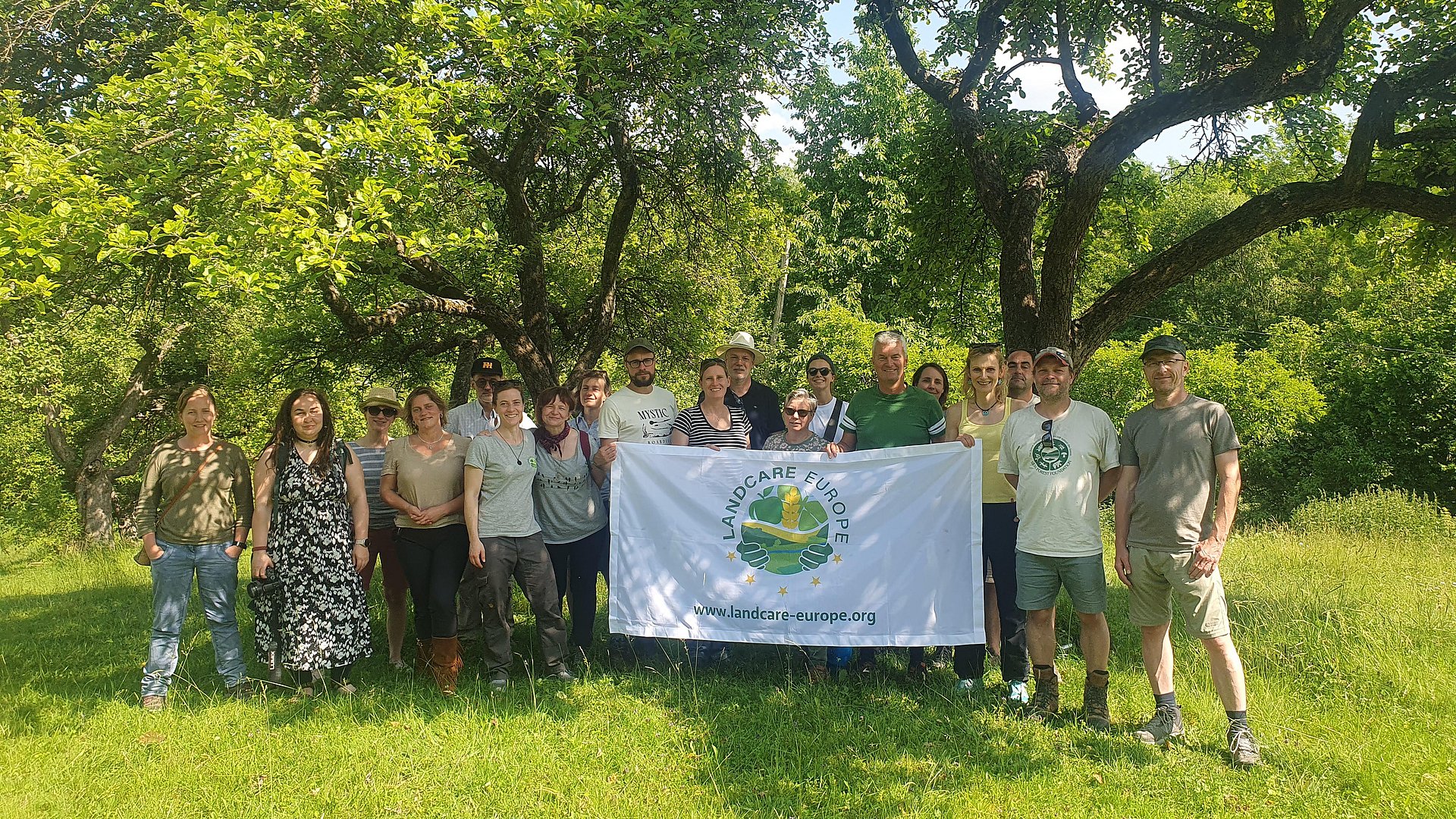 Group of people standing in front of trees holding a flag with the Logo of Landcare Europe